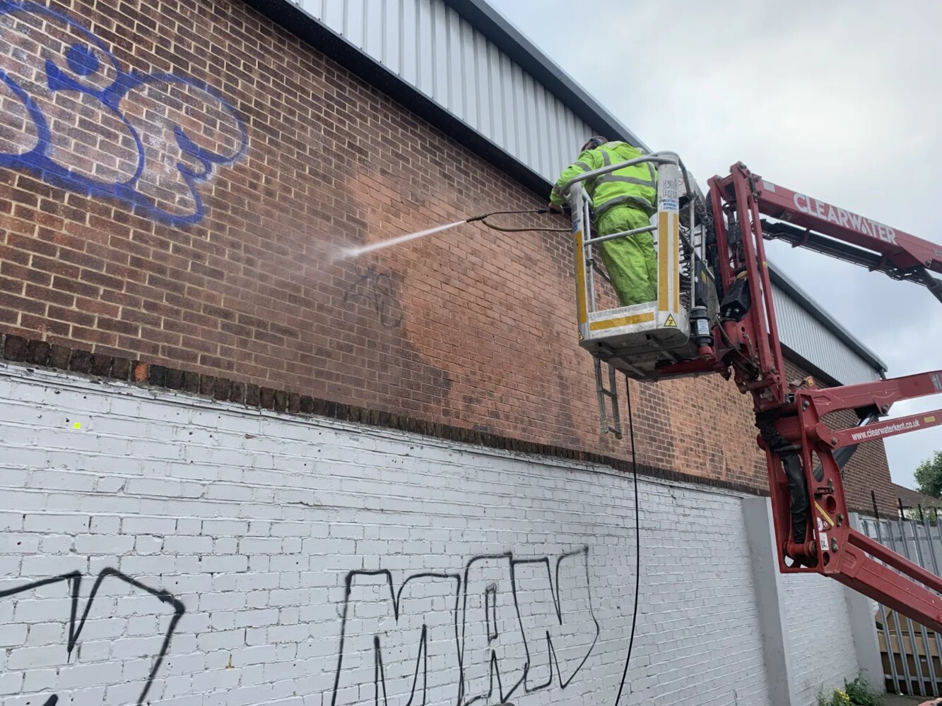 Worker removing graffiti from brick wall
